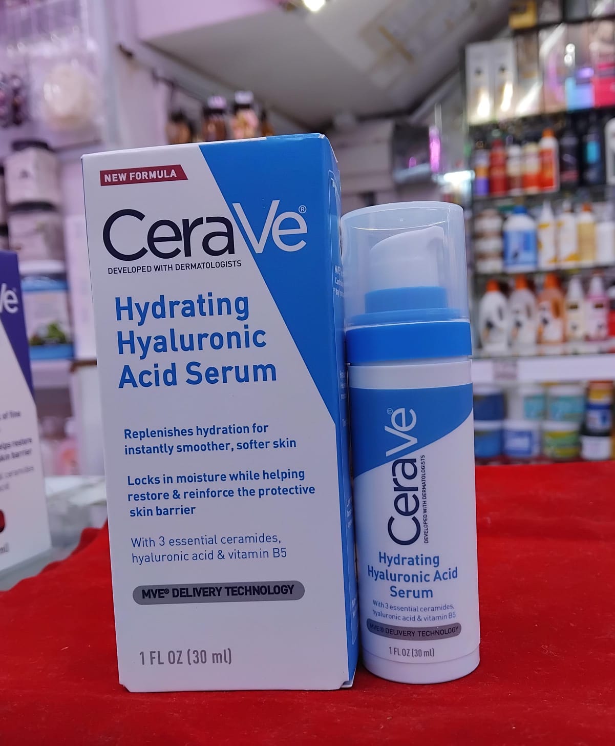 CeraVe Hydrating Hyaluronic Acid Serum packaging on a red surface with blurred store background