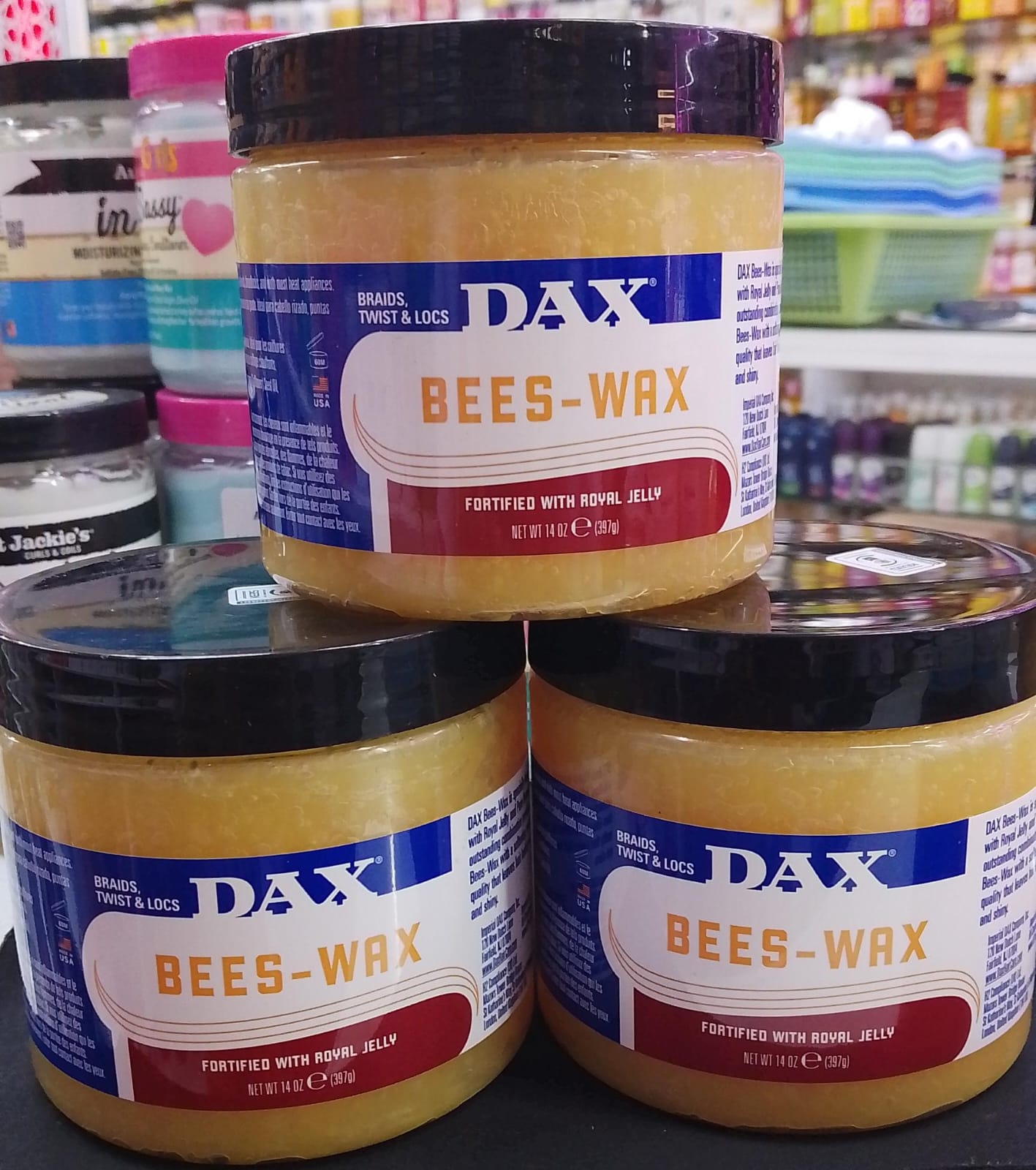 Three jars of Dax Bees-Wax on a store shelf with various products in the background.