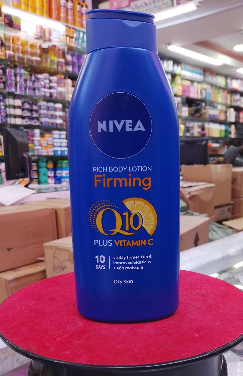 Nivea Q10 Plus Vitamin C body lotion bottle on a red surface with a store background.