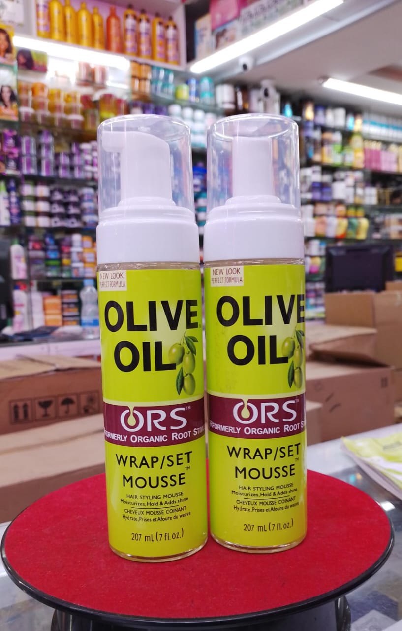 Two bottles of ORS Olive Oil Wrap/Set Mousse on a red surface with a store shelf in the background.