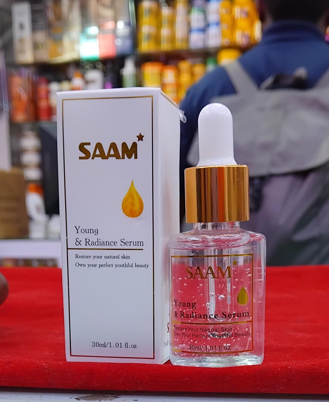 SAAM Young & Radiance Serum bottle and packaging on a red surface with blurred background