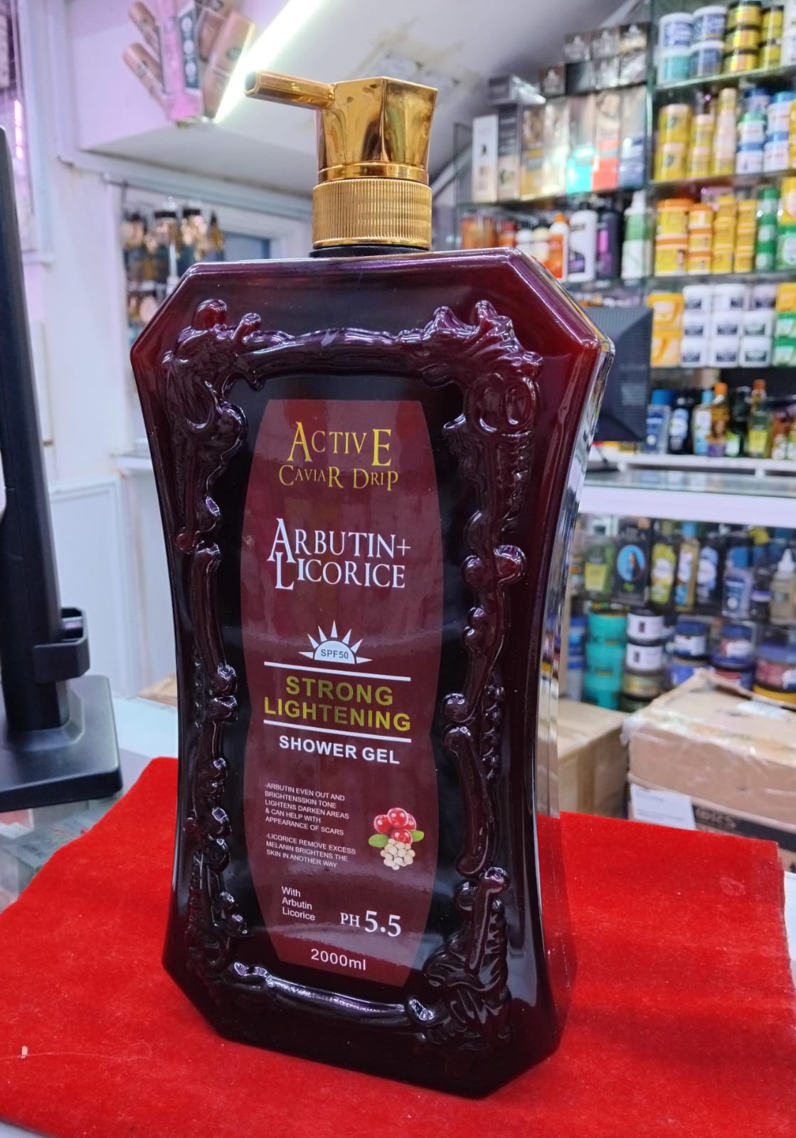 Bottle of Arbutin + Licorice shower gel on a red surface with a store shelf in the background.