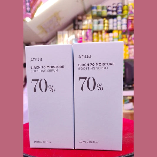 Two boxes of Anua Birch 70 Moisture Boosting Serum on a red surface with a blurred store background.