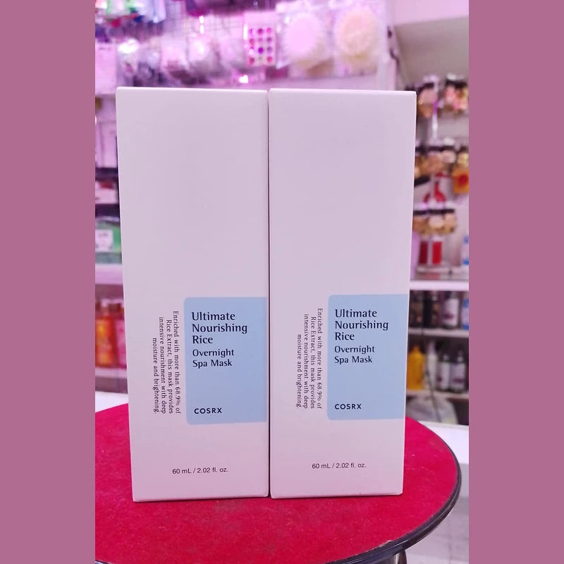 Two boxes of COSRX Ultimate Nourishing Rice Overnight Spa Mask on a red surface with a blurred store background.