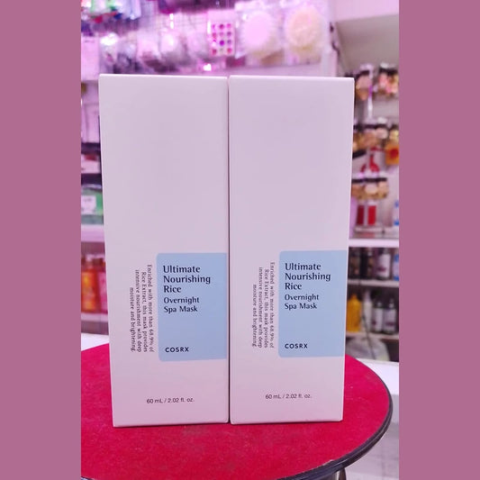 Two boxes of COSRX Ultimate Nourishing Rice Overnight Spa Mask on a red surface with a blurred store background.