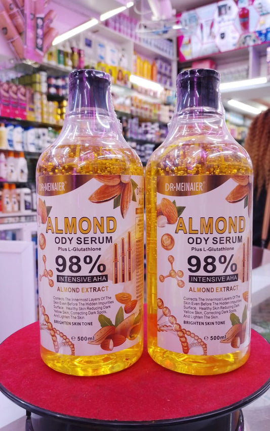 Two bottles of almond body serum on a red surface with a store shelf in the background.