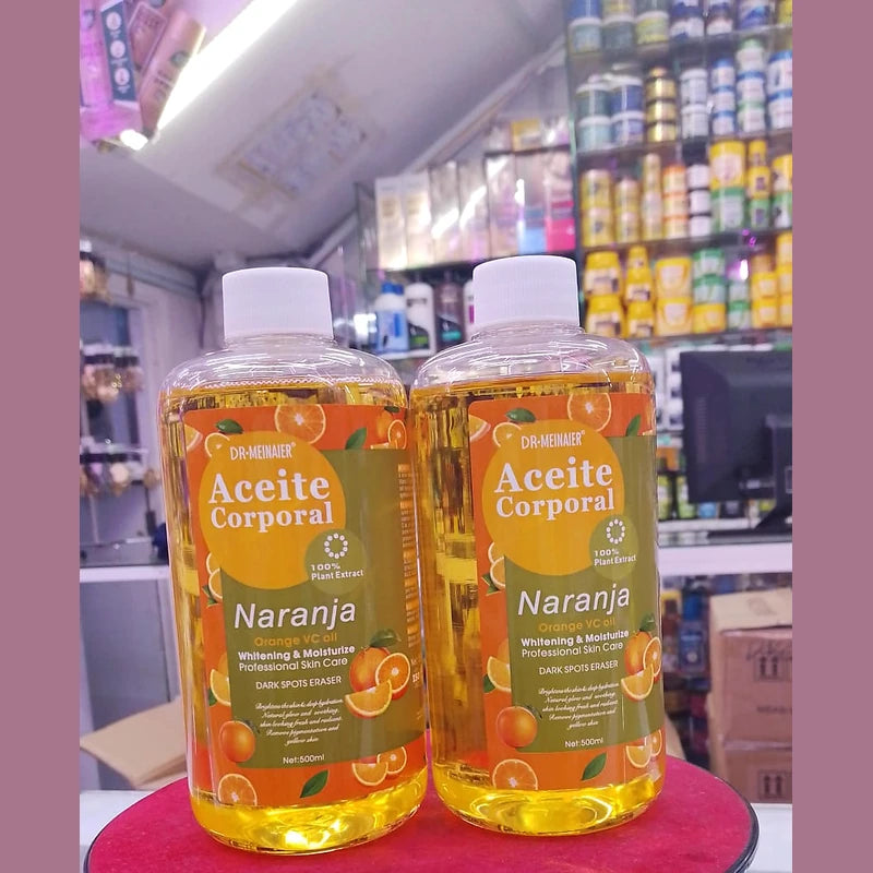 Two bottles of 'Aceite Corporal Naranja' on a red surface with a store shelf in the background.