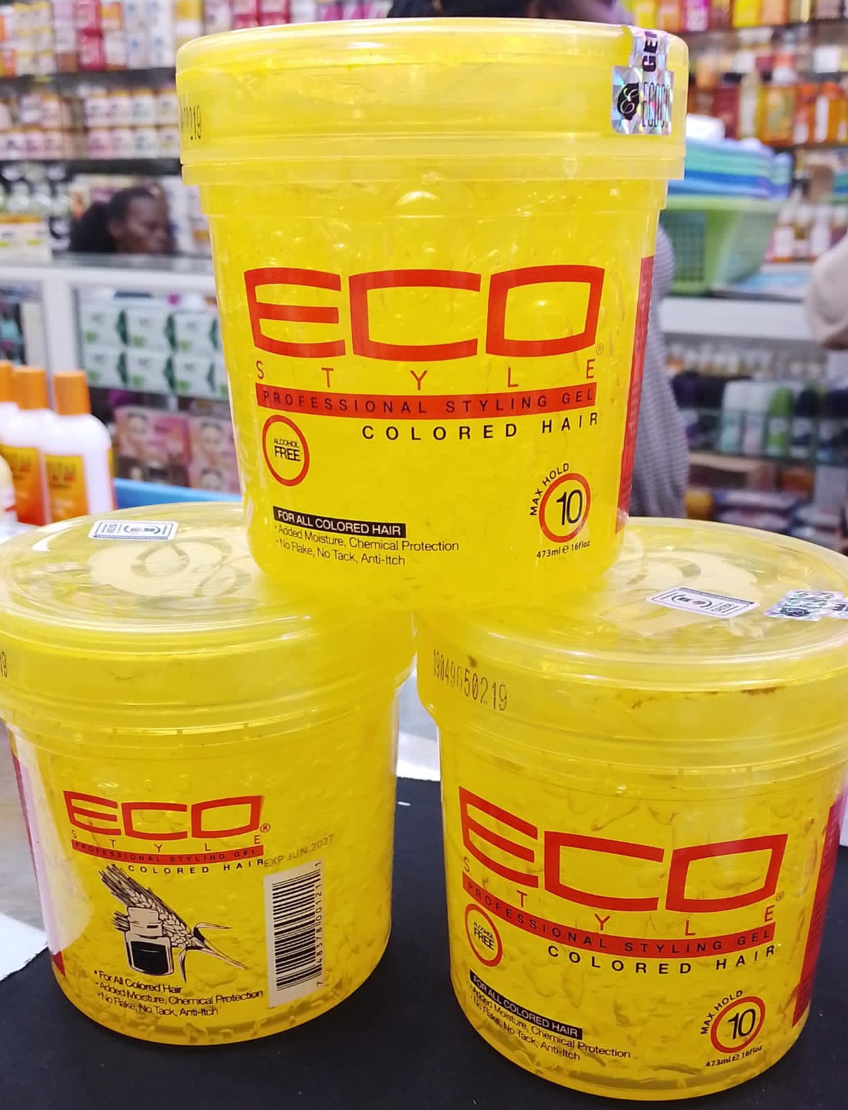 Three yellow containers of Eco Style hair product on a shelf in a store.