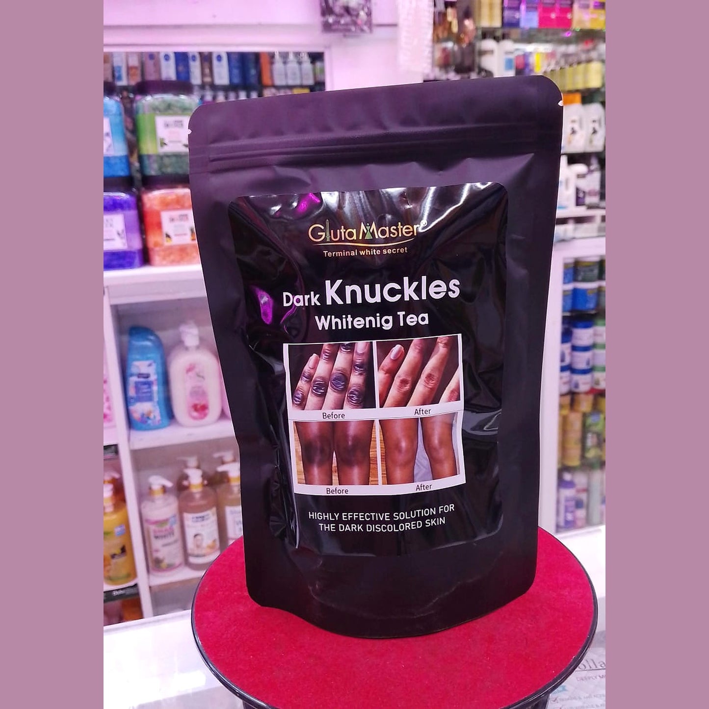 Black package of 'Dark Knuckles Whitening Tea' on a red stand with a store shelf in the background.