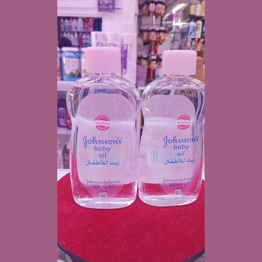 Two bottles of Johnson's baby oil on a red surface with a store shelf in the background.