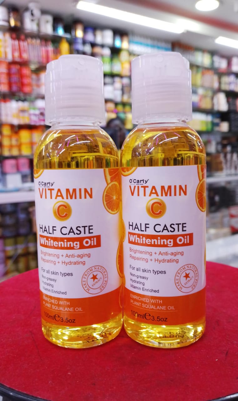 Two bottles of Half Caste Vitamin C Whitening Oil on a store shelf.