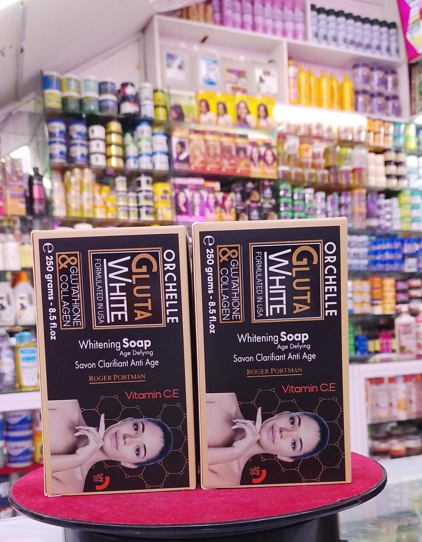 Two boxes of Orchelle Gluta White Whitening Soap on a pink stool with a store shelf in the background.