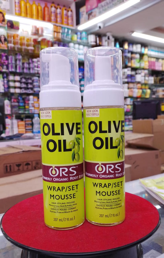 Two bottles of ORS Olive Oil Wrap/Set Mousse on a red surface with a store shelf in the background.