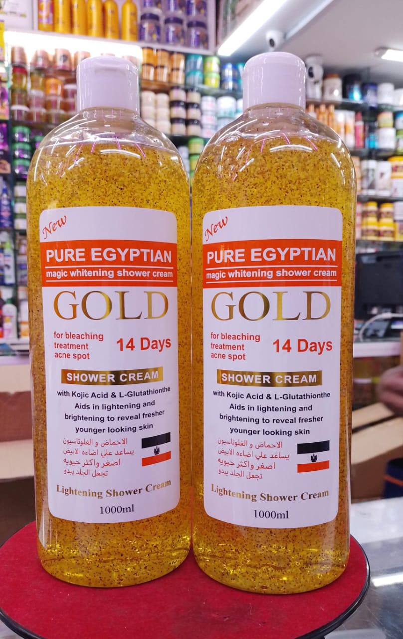 Two bottles of Pure Egyptian Gold Shower Cream on a red surface with a blurred store background.