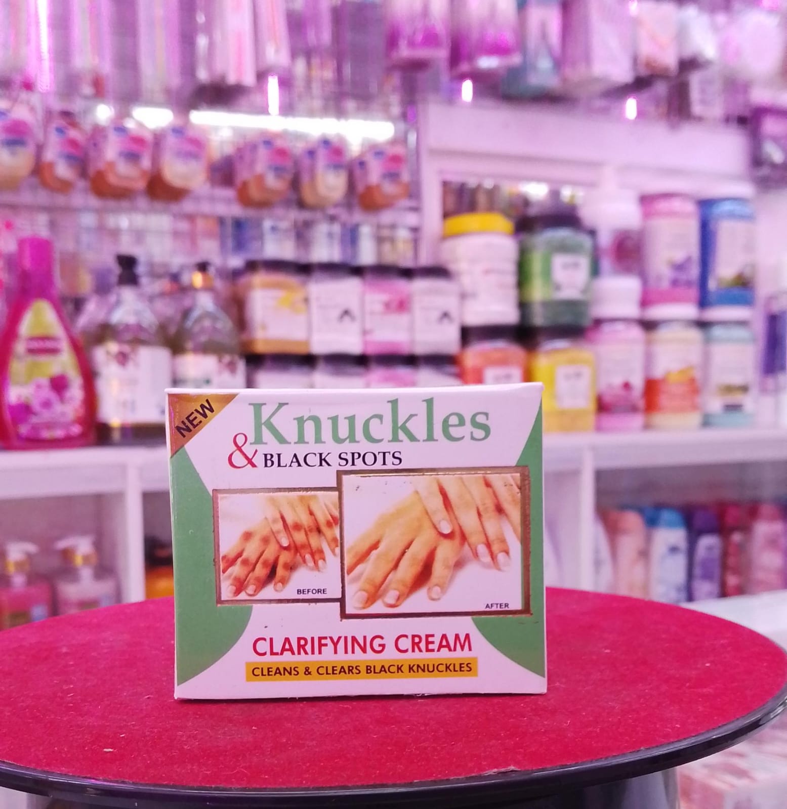Knuckles and Black Spots clarifying cream packaging on a red surface with a blurred store background.