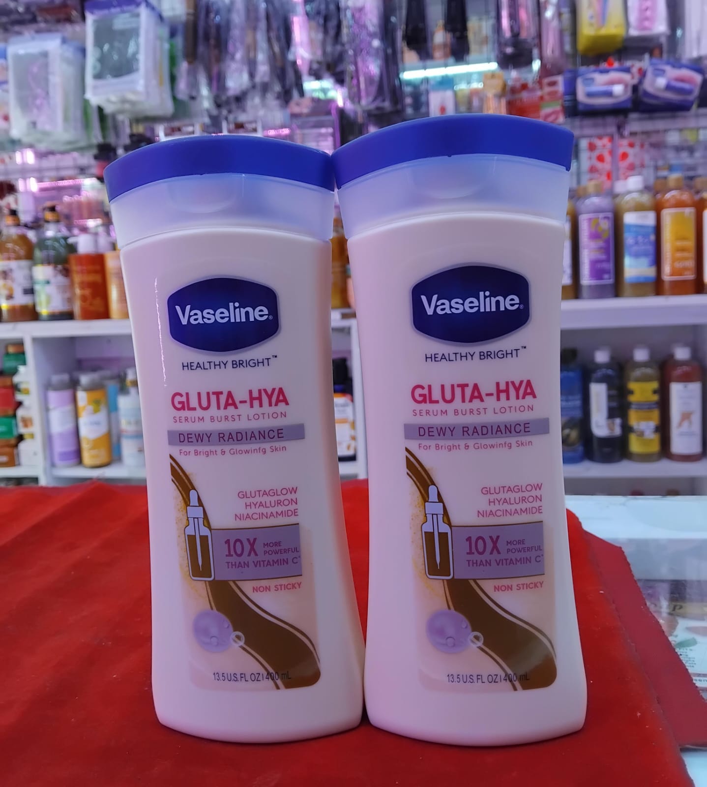 Two bottles of Vaseline Gluta-Hya lotion on a red surface with a store shelf in the background.