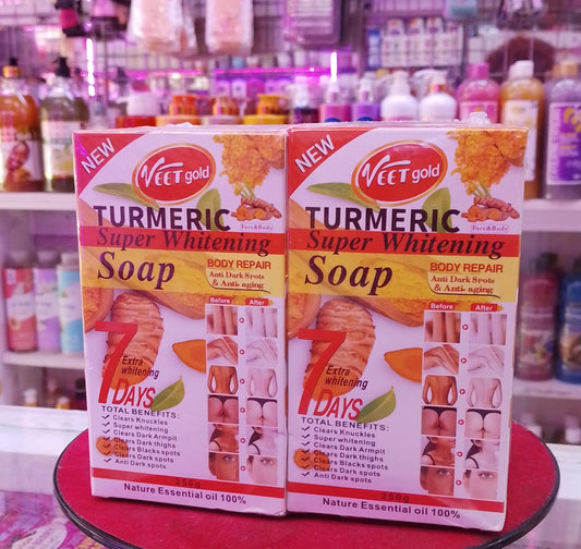 Two boxes of Veet gold Turmeric Super Whitening Soap on a red surface with a blurred store background.
