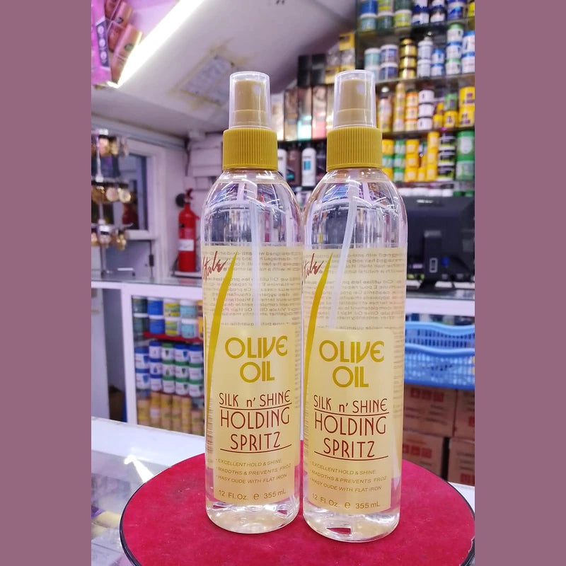 Two bottles of Olive Oil Silk 'n Shine Holding Spritz on a red surface with a store shelf in the background.